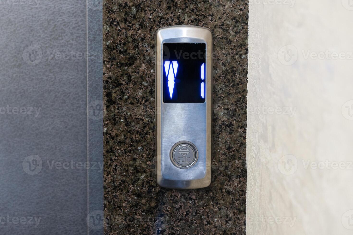 A stylish elevator control panel features a digital display, glowing with blue lights, set against a sleek stone wall in an upscale building photo