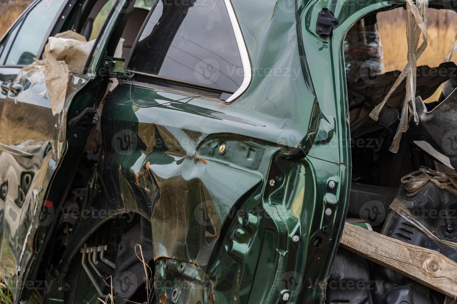 The wrecked green vehicle sits in a rural area, displaying severe dents and torn materials from an accident, surrounded by nature photo
