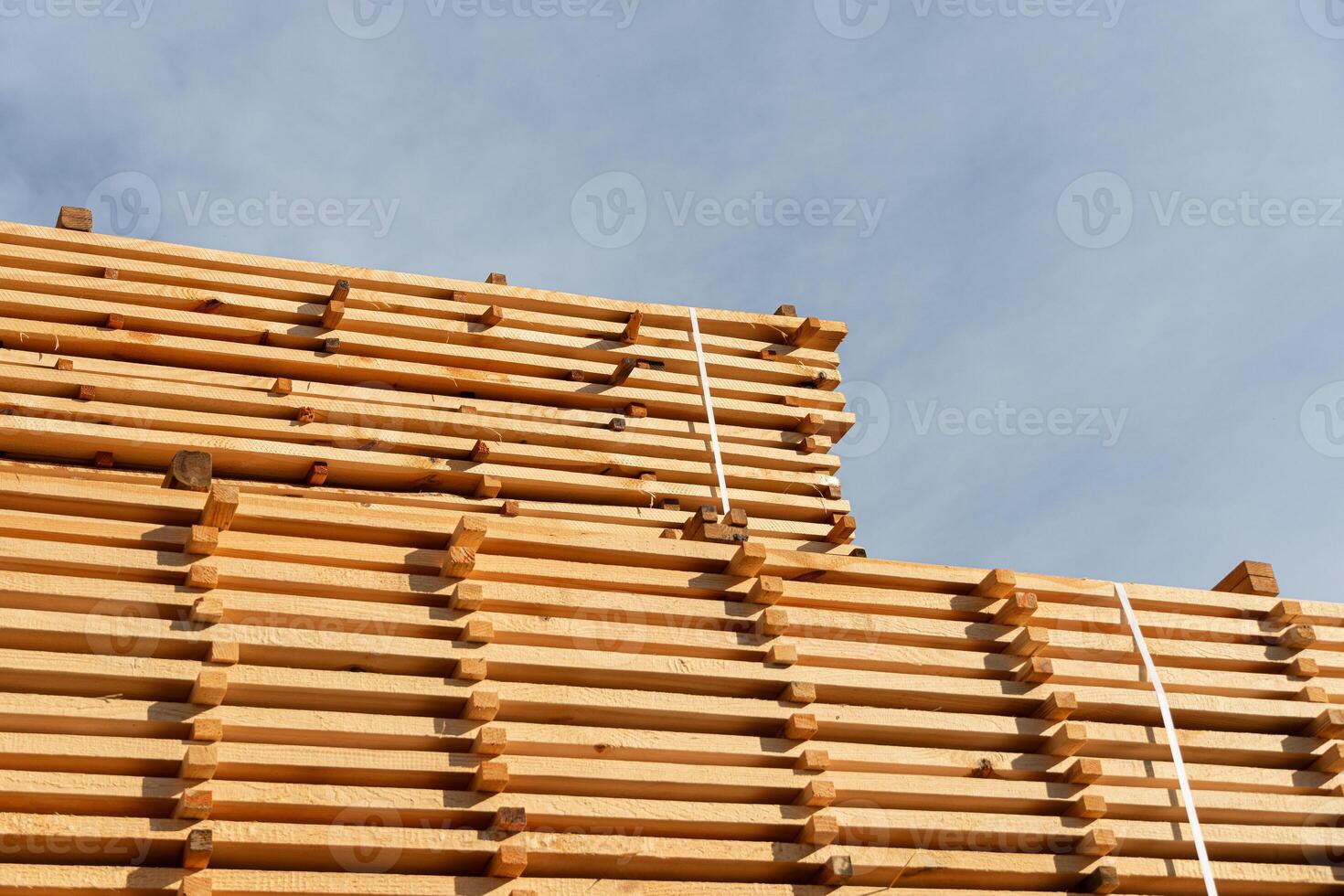 Tall stacks of new timber are neatly organized against a backdrop of a bright blue sky, showcasing the beauty of natural materials photo