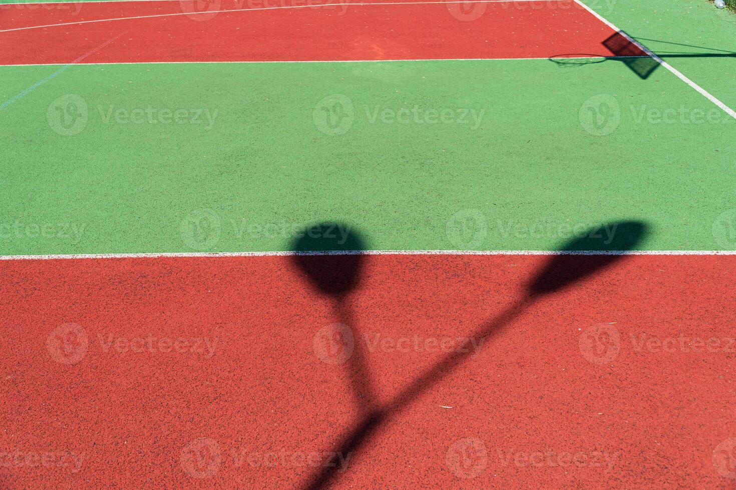 Striking shadows cast by nearby poles mingle with the bright colors of a freshly maintained tennis court on a sunny day photo