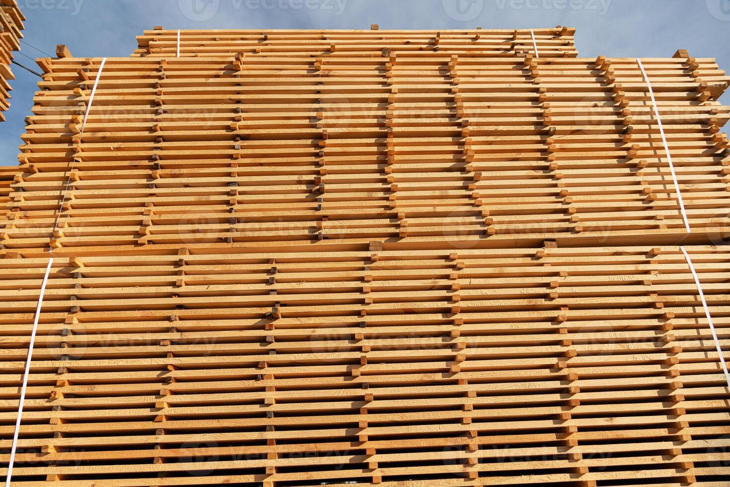 Tall stacks of neatly arranged wooden planks glimmer under the bright sun, revealing the intricate details of woodworking techniques photo
