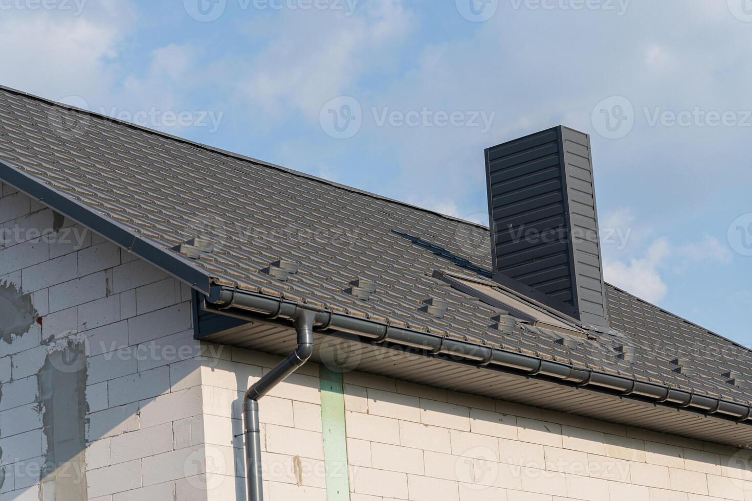 Newly constructed home featuring a gray roof and chimney against a clear sky, showcasing modern architecture and design elements photo