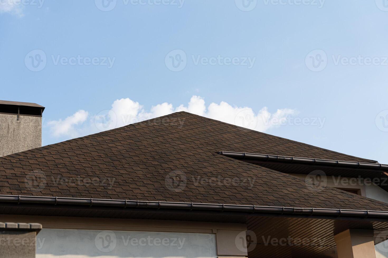 The roof of a contemporary house is highlighted against a bright blue sky with a few soft clouds visible above photo