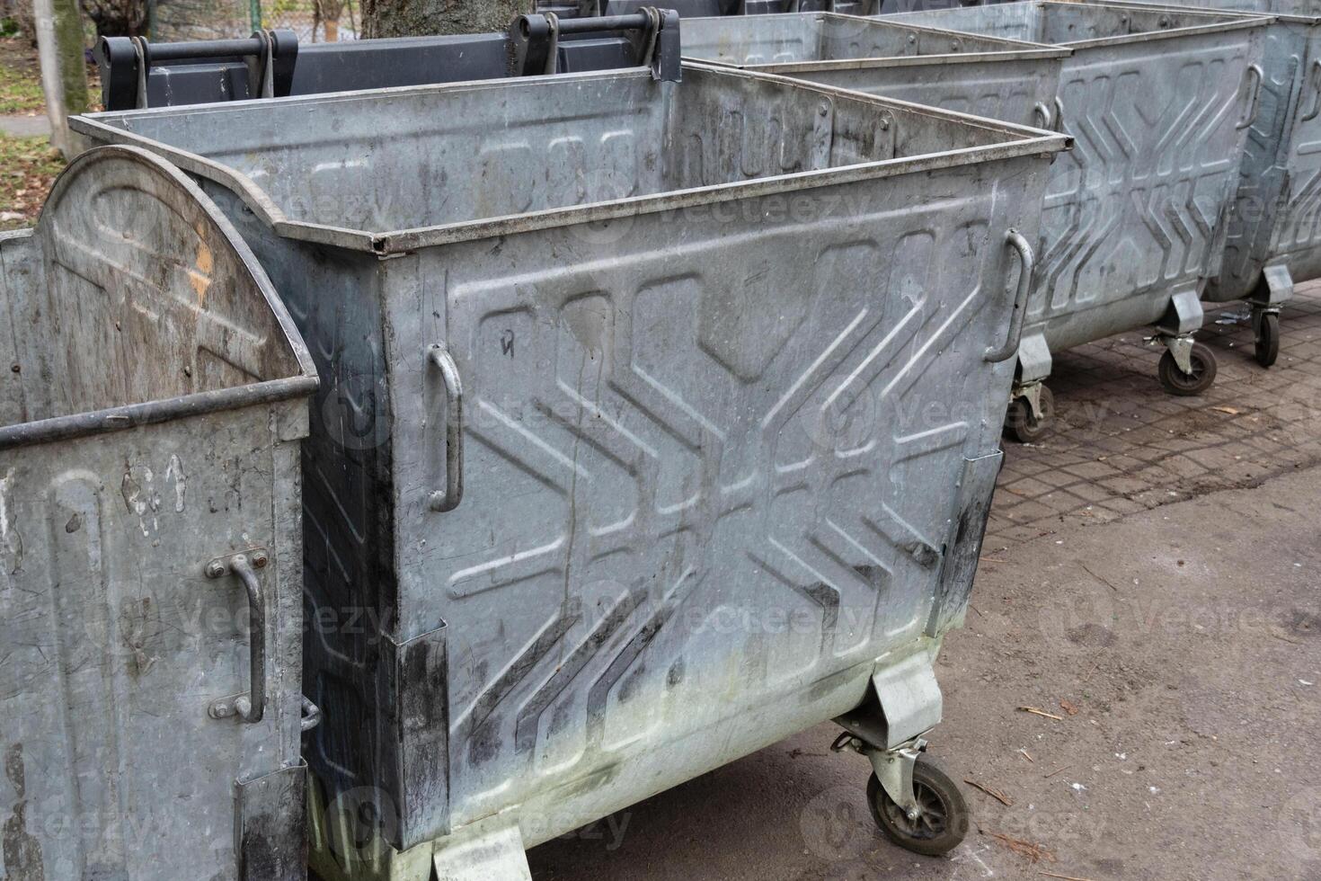 Multiple metal waste bins stand side by side on a city street, showing signs of use and wear in the afternoon light photo
