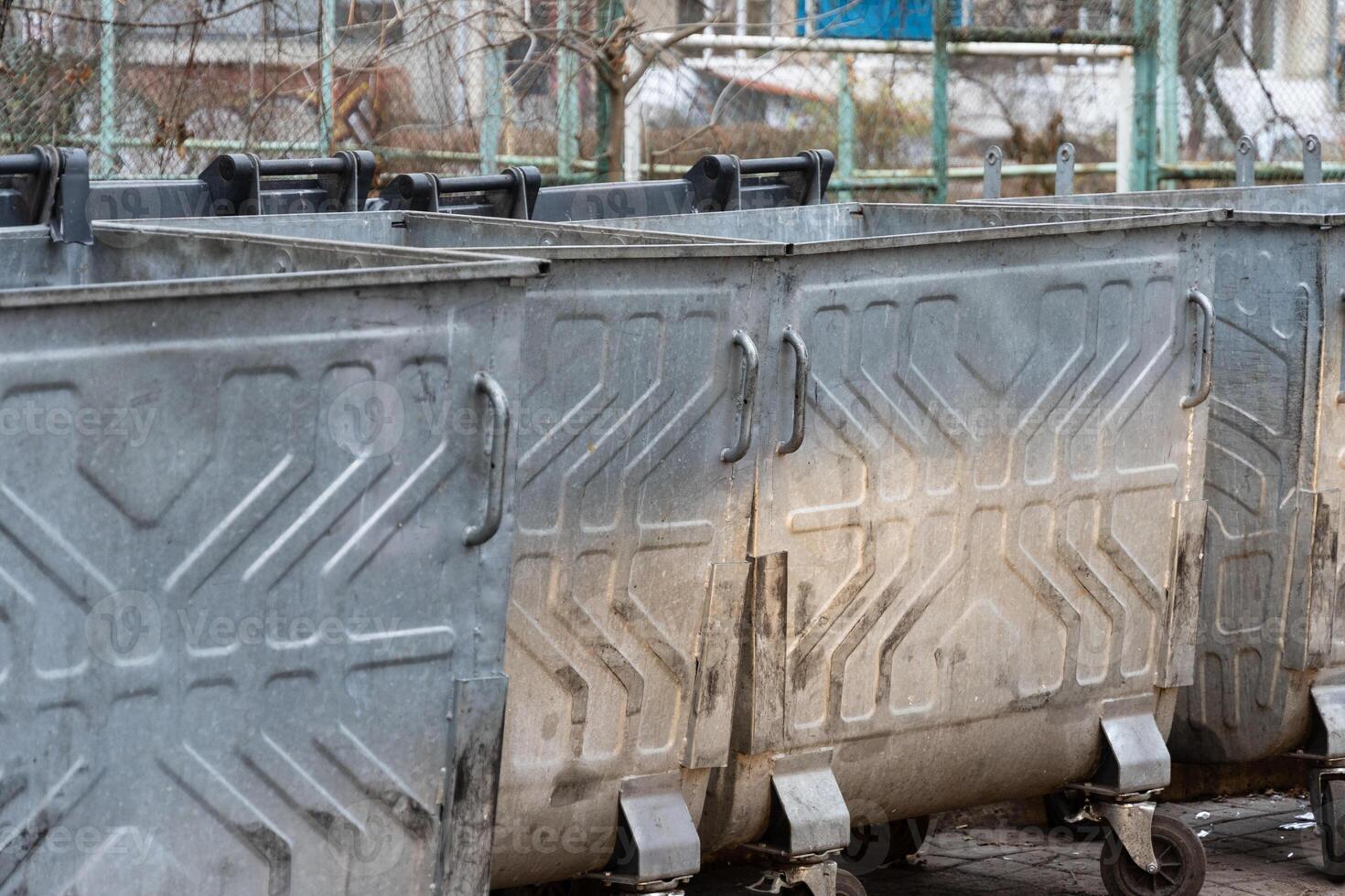 Several large metal waste containers are lined up in a park area, indicating a focus on waste management in an urban environment photo