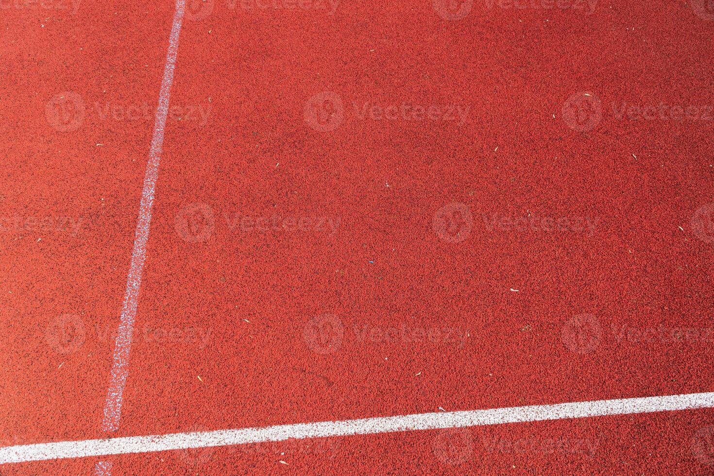 Red rubberized track with white lane markings under clear skies surrounded by natural elements during daylight hours photo