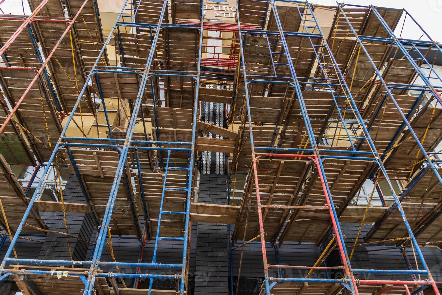 Workers utilize scaffolding to renovate a multi-story building in an urban area under clear skies, showcasing construction progress photo