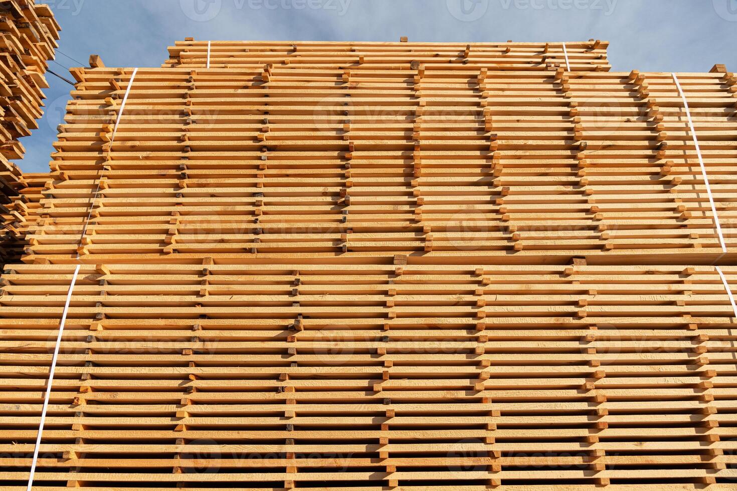Numerous wooden planks are neatly stacked in a lumber yard showcasing their natural grain and color under clear blue skies photo