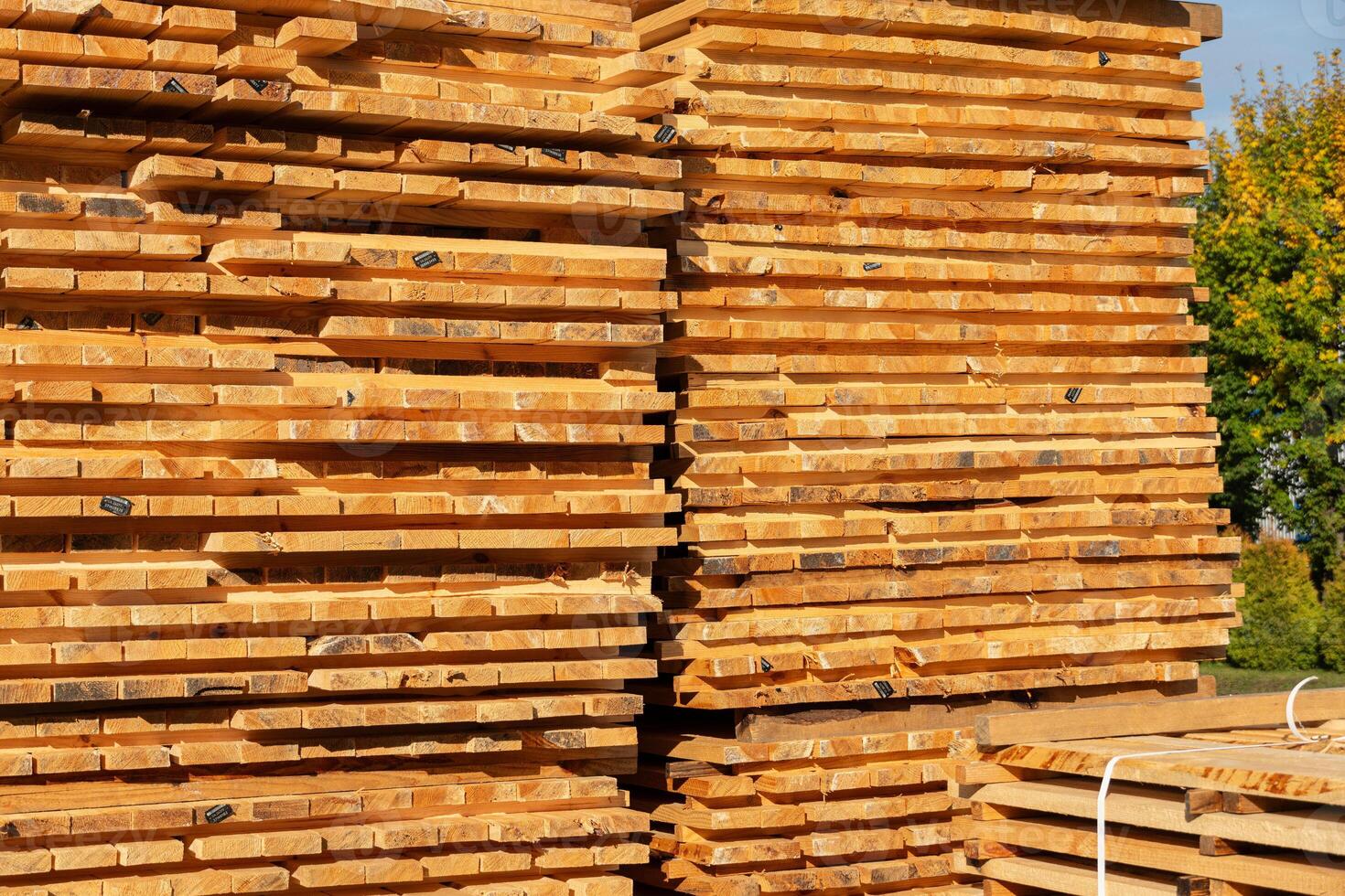 Stacks of freshly cut lumber showcase a variety of wooden planks under clear blue skies in a yard during the afternoon photo
