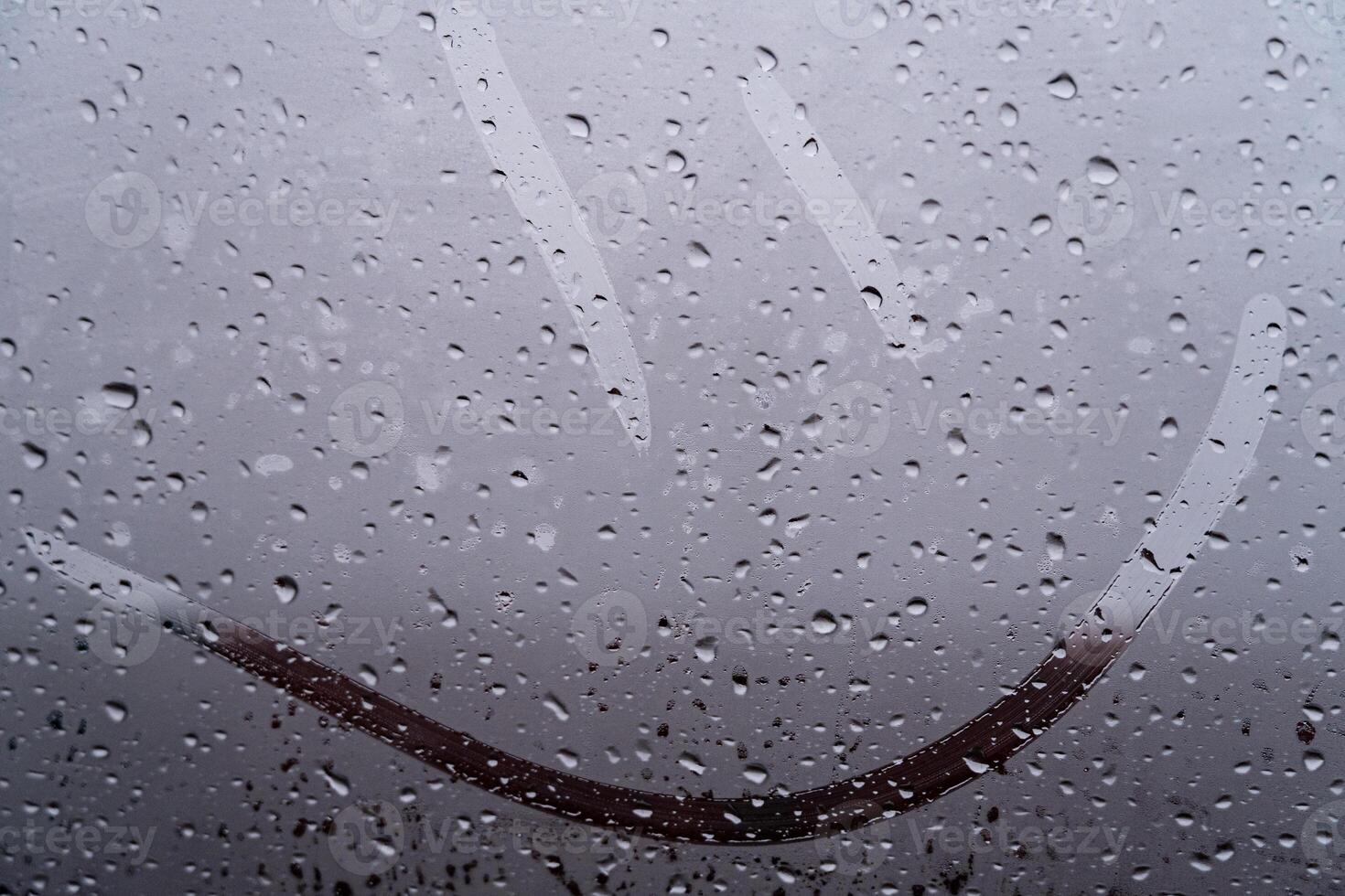A joyful smiley face artfully etched on a fogged glass window is surrounded by raindrops, bringing warmth to a dreary day photo