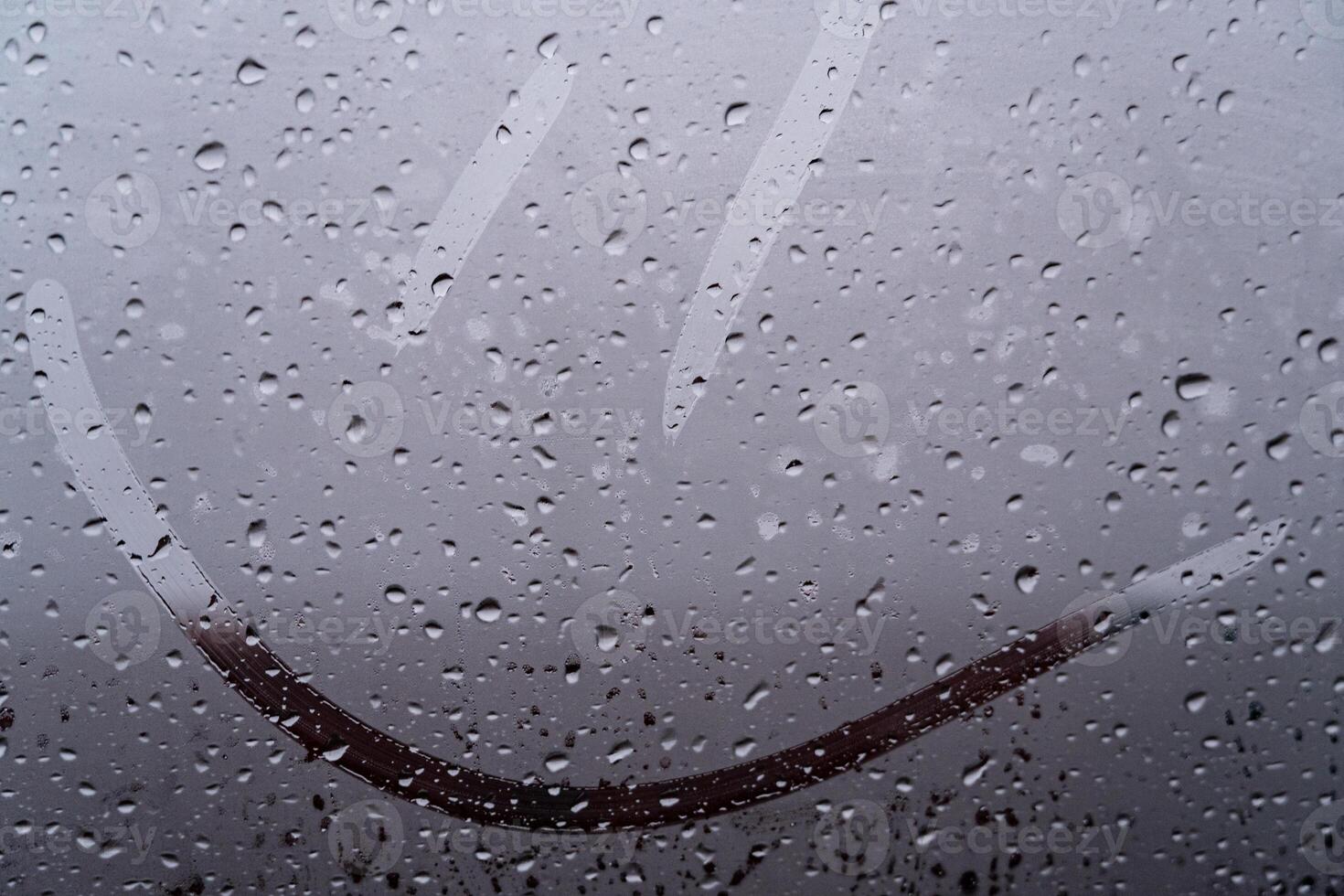 Cheerful smiley face etched on a foggy glass, surrounded by glistening raindrops. Nature's beauty brings moments of joy during rain photo