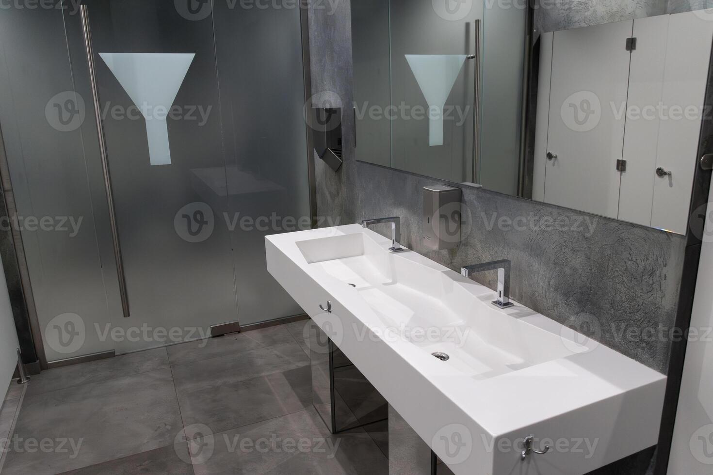 Contemporary restroom showcasing a spacious design with minimalist aesthetics, emphasizing cleanliness and functionality for public use photo