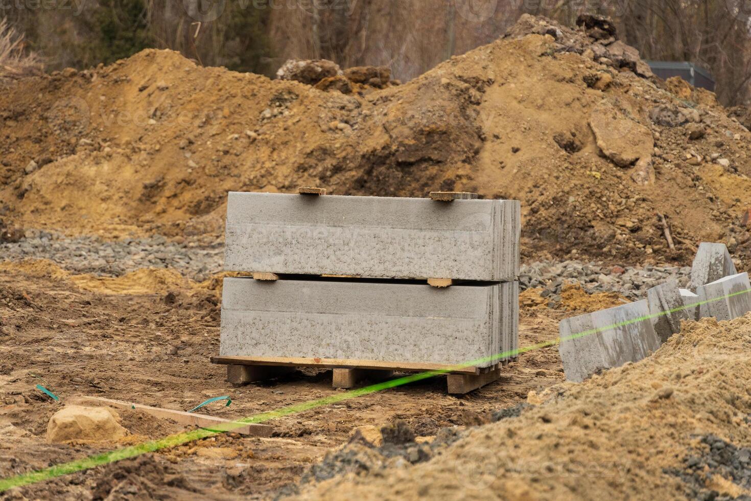 Workers are busy at a construction site, organizing concrete blocks on a gravel surface surrounded by heavy machinery and earth photo