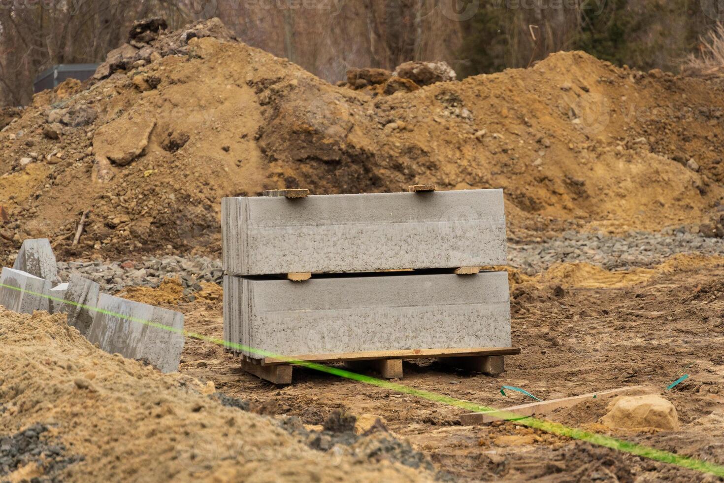 Concrete blocks are stacked on a pallet beside a gravel surface, indicating ongoing road repair and construction activities in an urban area photo