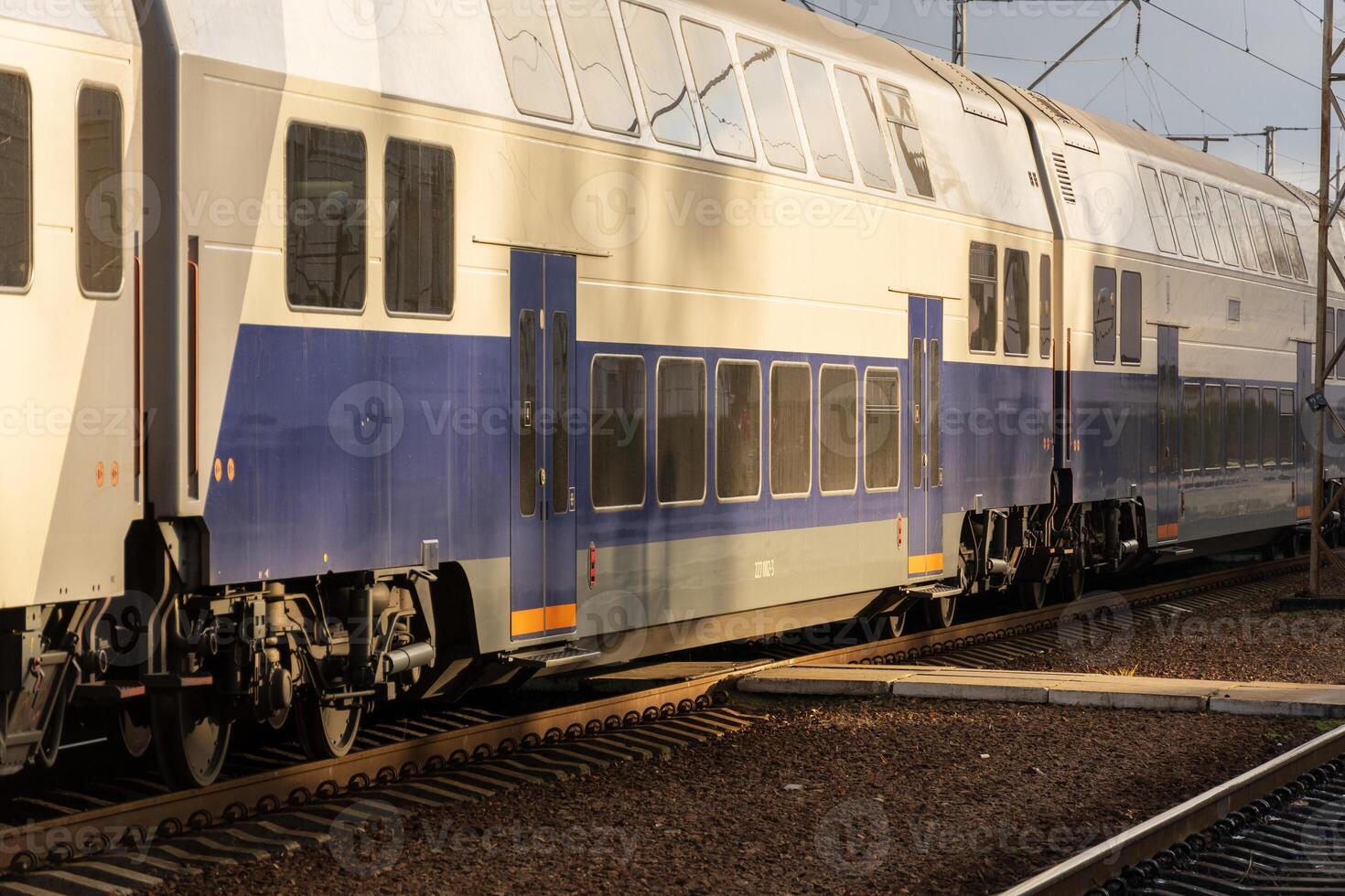 A sleek, double-decker electric train pulls into a busy railway station platform as sunlight bathes the scene in warm tones photo