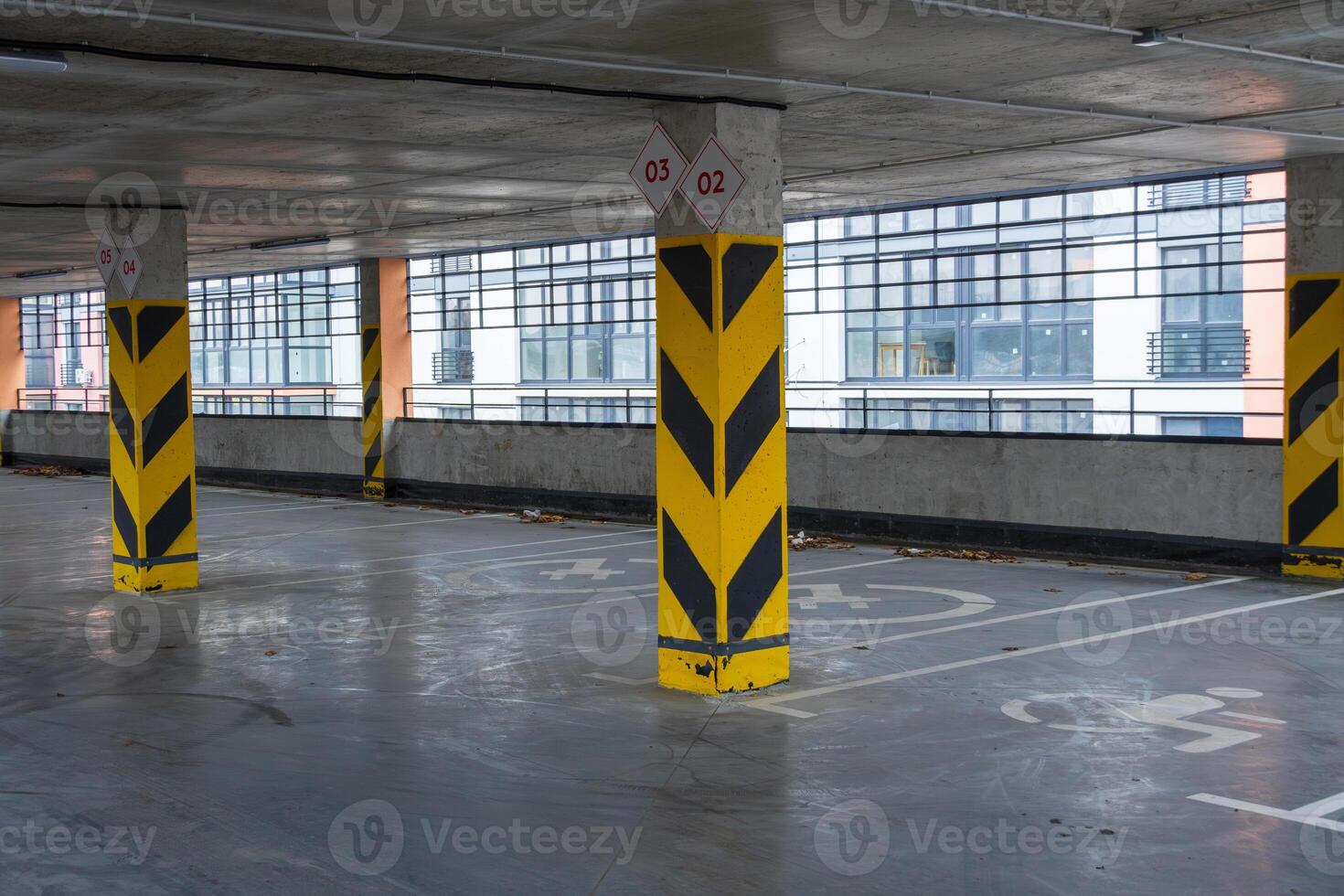Spacious underground parking garage featuring marked parking spaces and bold yellow pillars, providing a modern transport experience photo