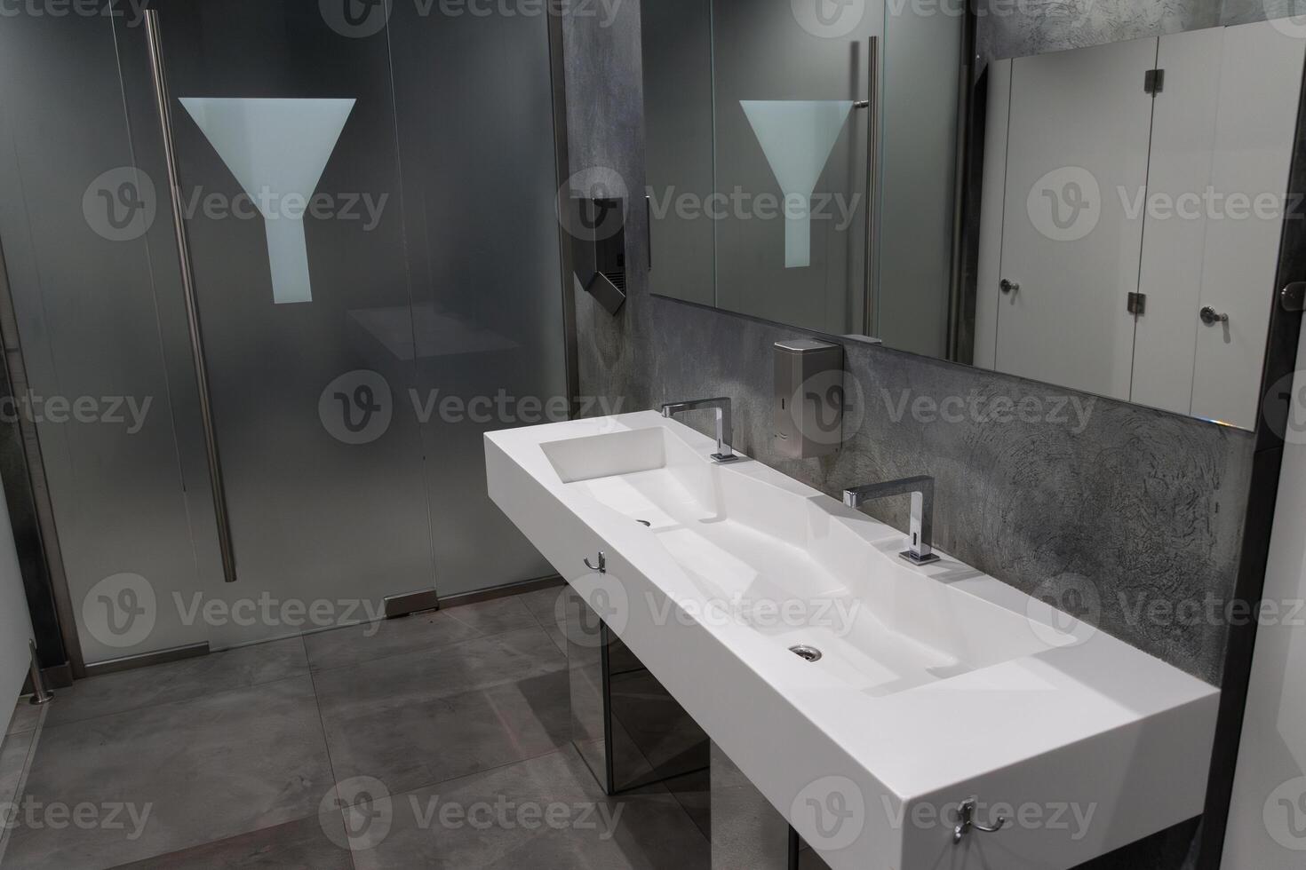 A contemporary bathroom showcases a clean, spacious design with dual sinks, sleek faucets, and frosted glass in an urban interior photo
