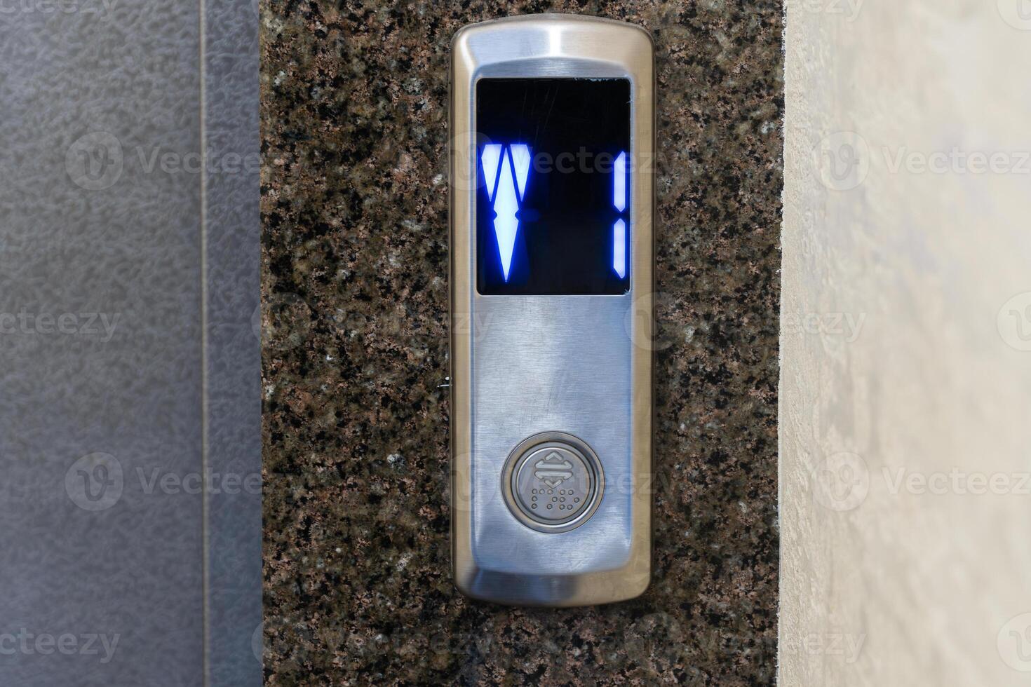 The control panel of a steel elevator displays illuminated numbers, showing current floor and direction in an apartment setting photo