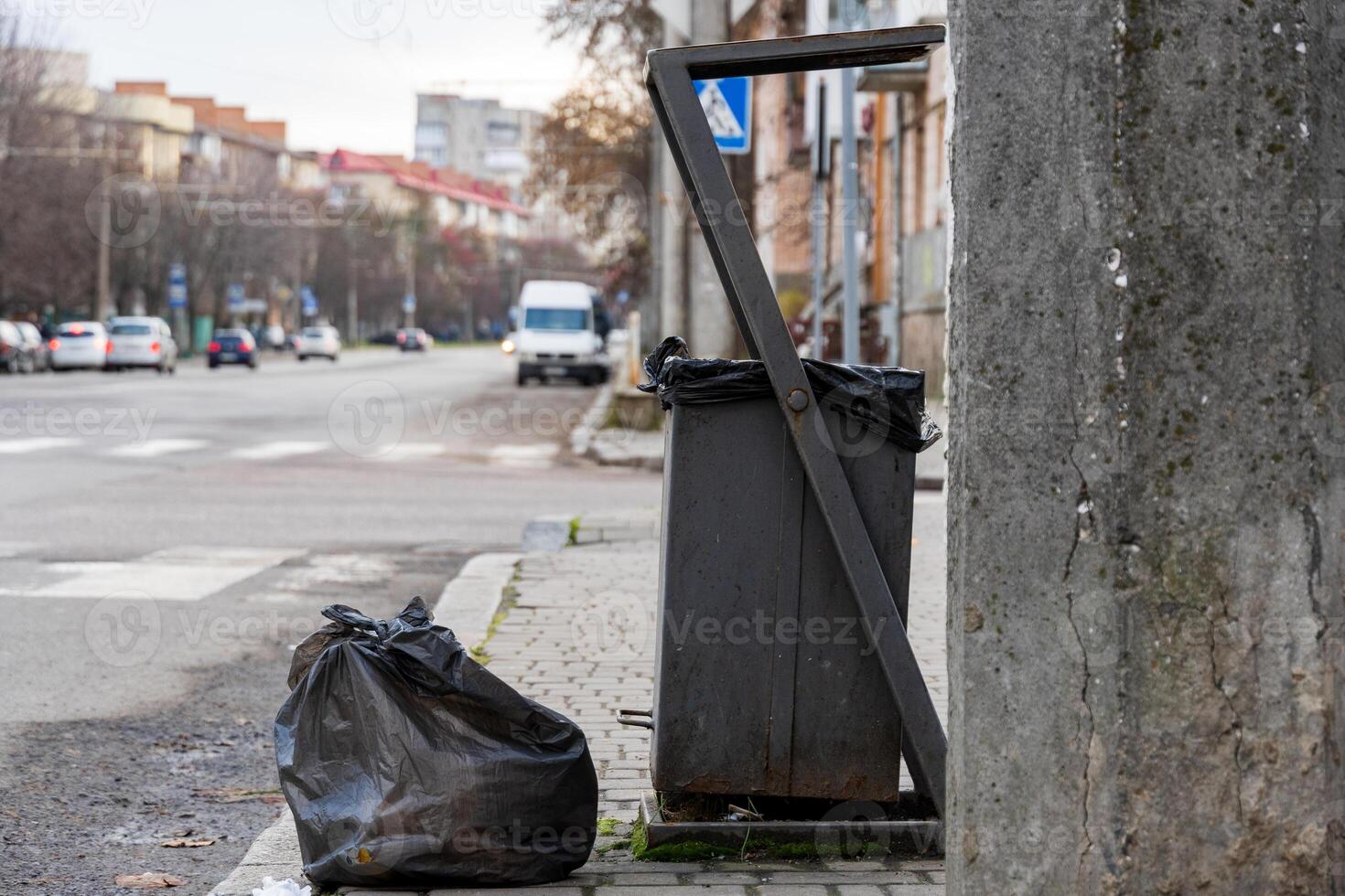 A garbage container stands near the sidewalk, surrounded by black trash bags, highlighting urban waste management challenges photo