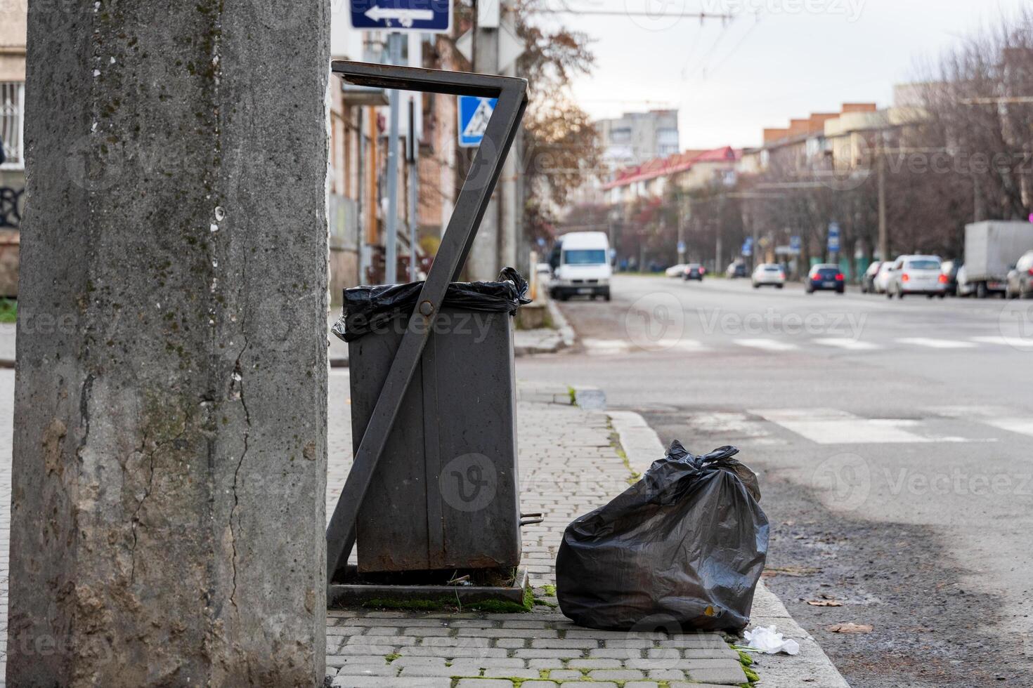 Trash bags stacked beside a refuse container on a city sidewalk demonstrate the ongoing issues of waste disposal and environmental care photo