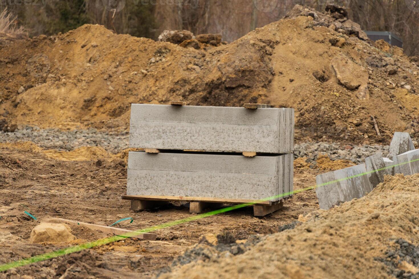 Stacks of concrete blocks sit on a pallet amidst gravel and dirt at a construction site along the city street with ongoing repair work photo