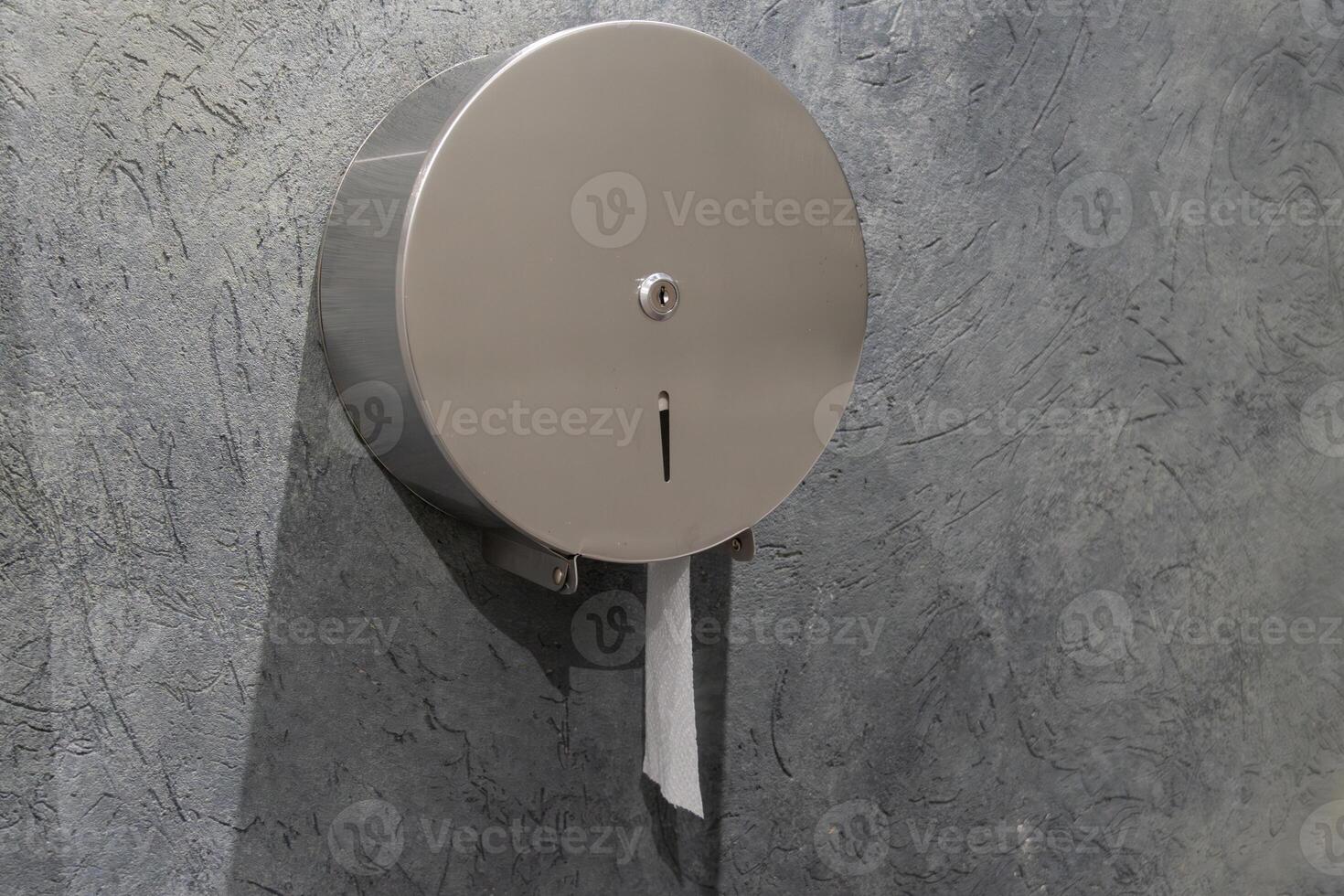 A round stainless steel toilet paper dispenser is installed in a gray wall, promoting hygiene and cleanliness in the restroom area photo