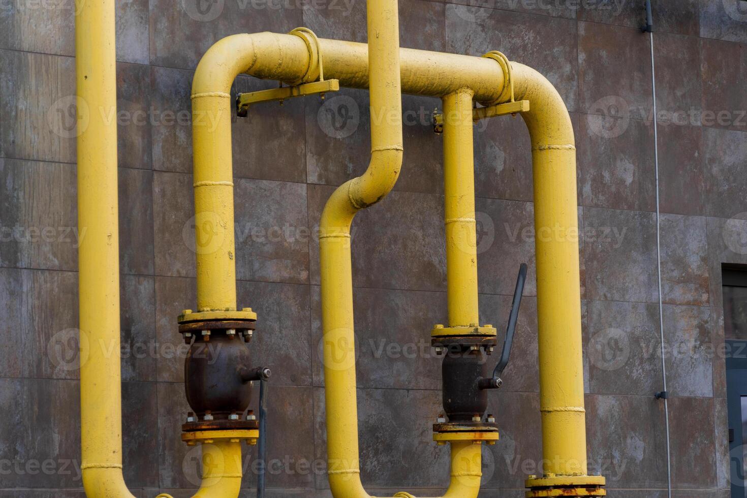 A network of yellow gas pipes connects to valves on a building's exterior, illustrating industrial energy transportation infrastructure photo