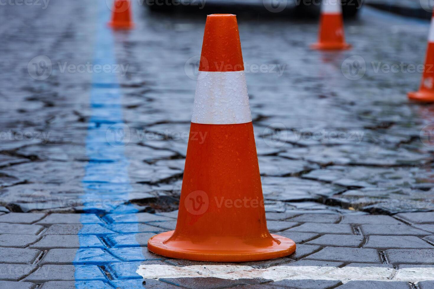 Traffic cones are set up in a temporary construction area, creating a safety zone amid wet cobblestones and rainy urban conditions photo