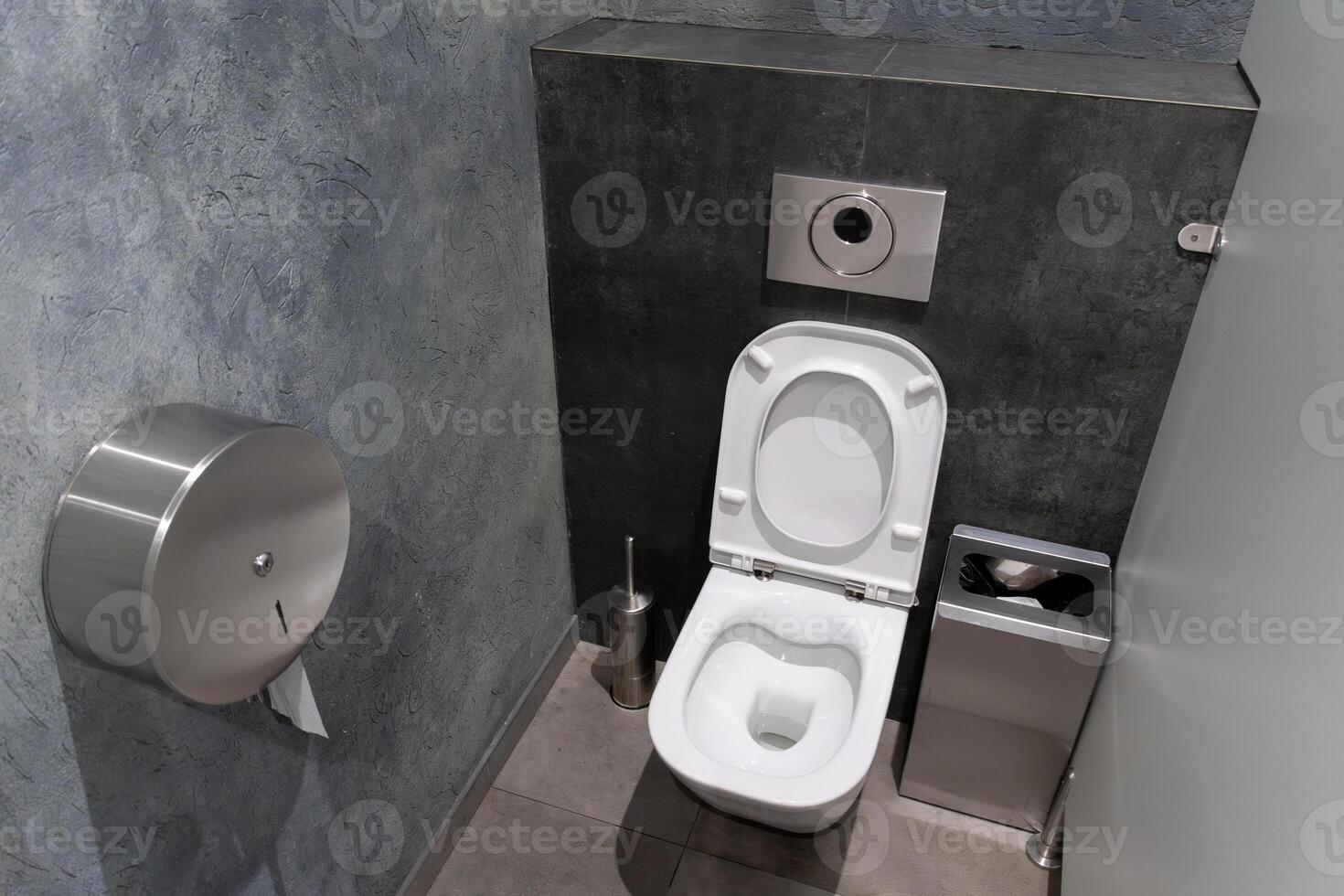 A modern restroom showcases a minimalistic toilet and efficient waste disposal unit against a backdrop of clean grey walls and sleek design photo