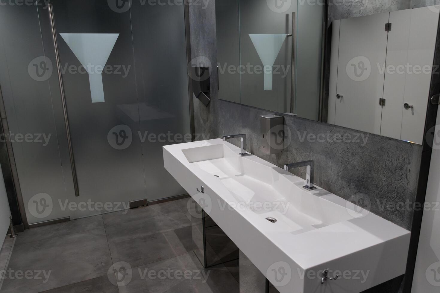 Spacious restroom showcases sleek frosted glass and a stylish dual sink with minimalist faucets, emphasizing hygiene and modern design photo