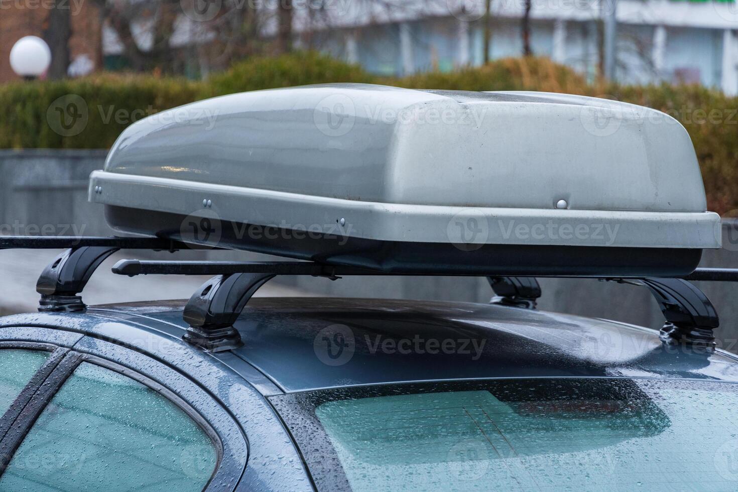 A sleek urban car rests in a parking area as evening rain falls, featuring a roof-mounted container designed for outdoor adventures photo