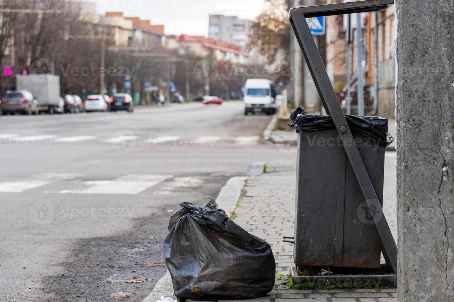 Black garbage bags left beside a recycling bin on a city street highlight the challenges of environmental conservation and waste disposal photo