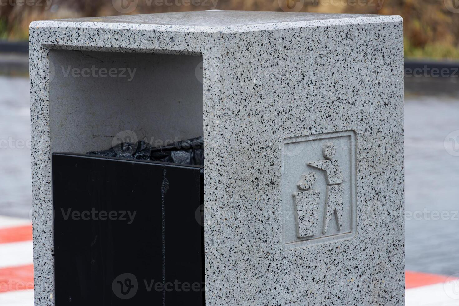 A concrete garbage container stands near water, promoting proper disposal of waste, including recycling and cigarette butts for clean surroundings photo