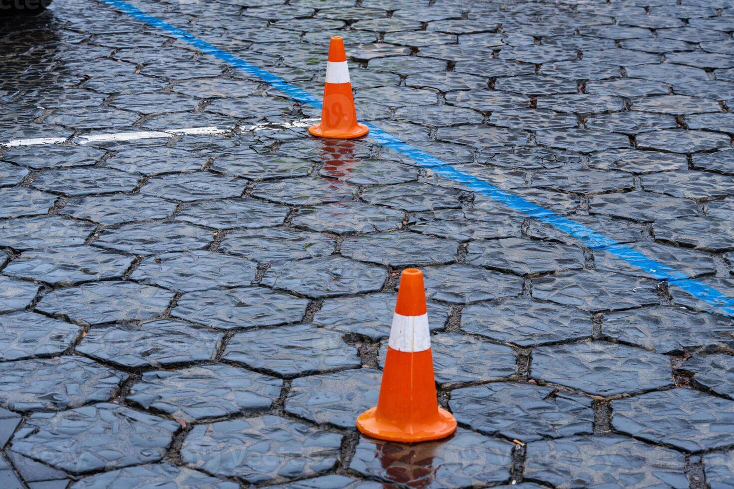 Traffic cones are placed in a construction zone on a cobblestone street, reflecting rainwater and highlighting urban roadworks photo