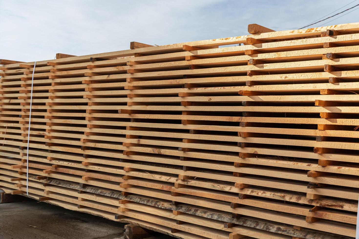 Freshly cut lumber is stacked and drying in the sun at a sawmill, showcasing the natural wood grain and warm tones in a rural setting photo
