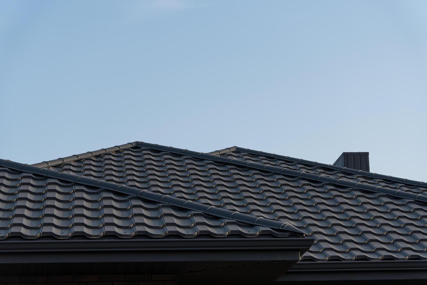 Two sloped roofs with gray tiles stand against a clear blue sky in a quiet suburban area during the afternoon photo