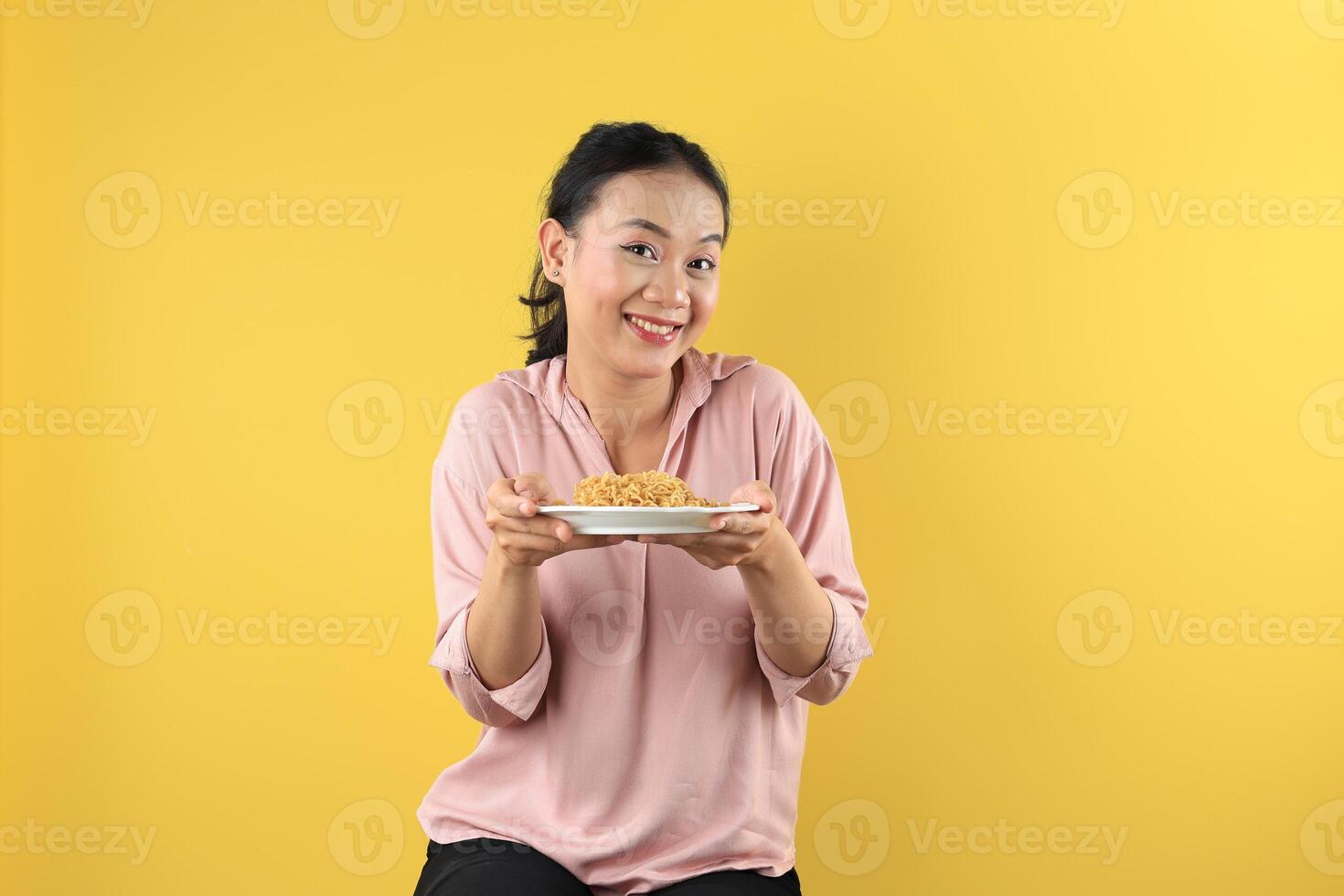 Asian Young Woman in Peach Shirt Holds a Plate of Mie Goreng Noodles with Happy Face. photo