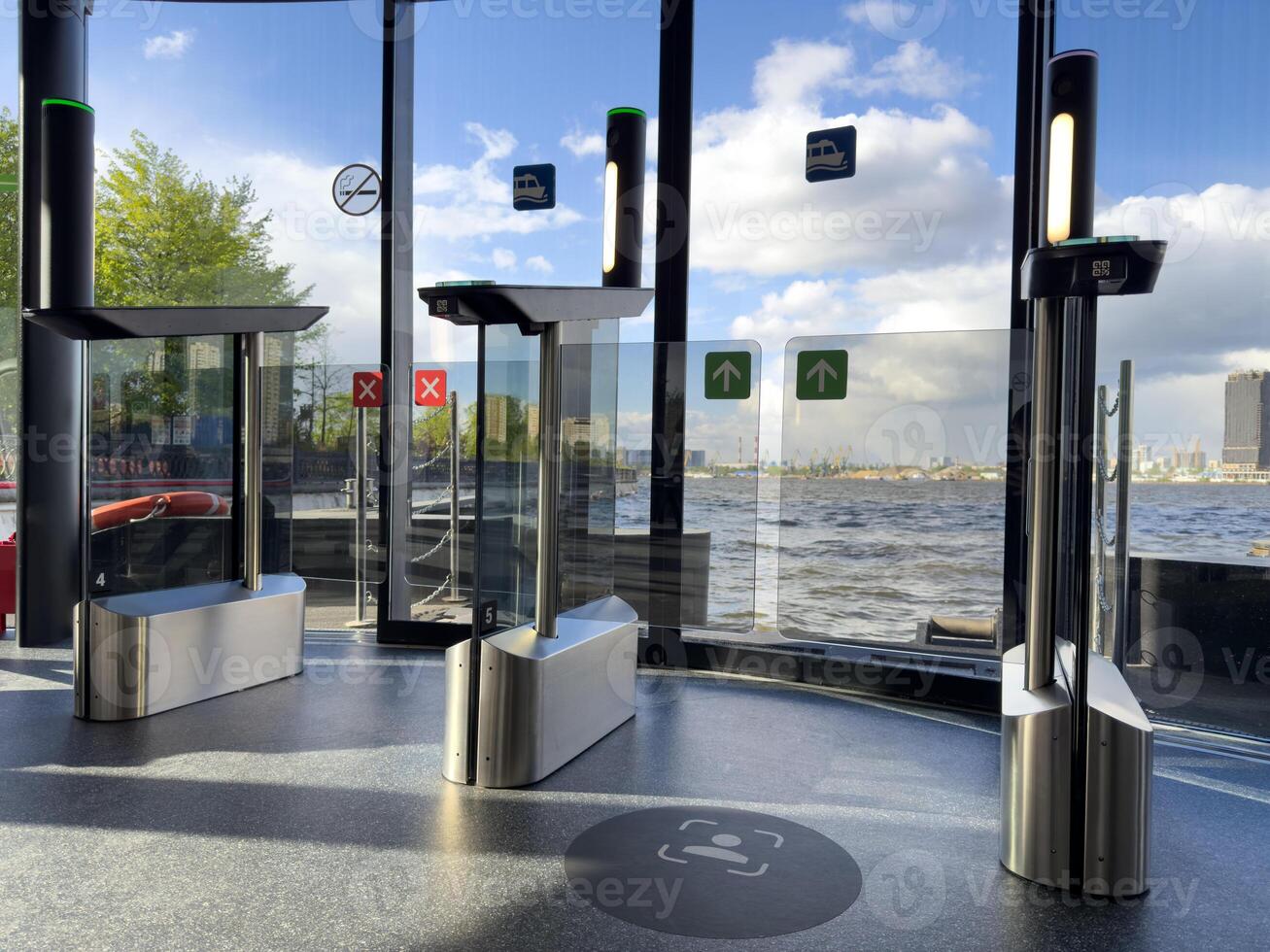Modern contactless turnstiles inside passenger river terminal with glass walls, water view and skyline. Touchless access system for public transport and smart city infrastructure. photo