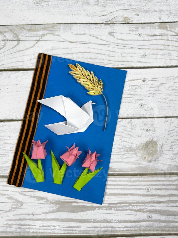 Victory Day card made from colored paper features red origami carnation flowers and Saint George ribbon. Symbolic tribute to the memory and heroism of World War II soldiers photo