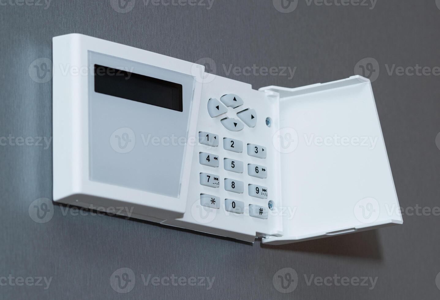 Security system keyboard with buttons and plastic cover mounted on a gray textured wall. photo