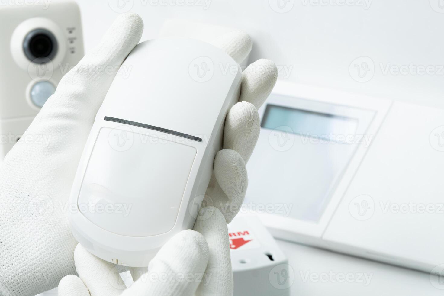 The left hand of a man in a white glove holds a motion sensor of security systems photo
