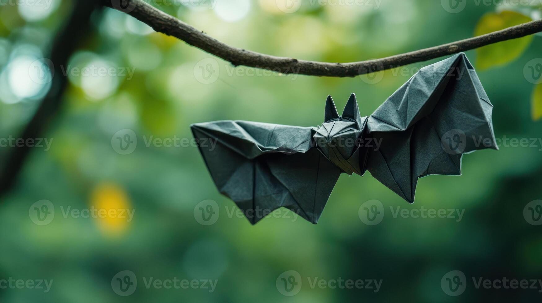 An origami bat is hanging from a small brown branch photo