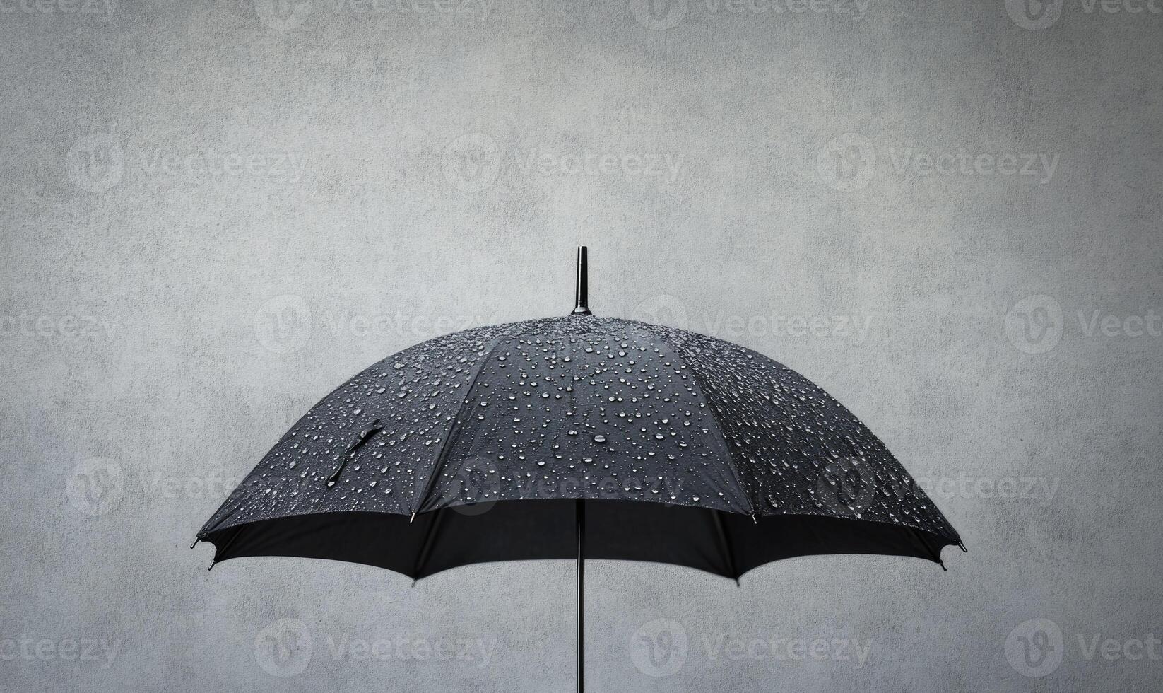 A black umbrella is open and has raindrops on it, gray wall background photo