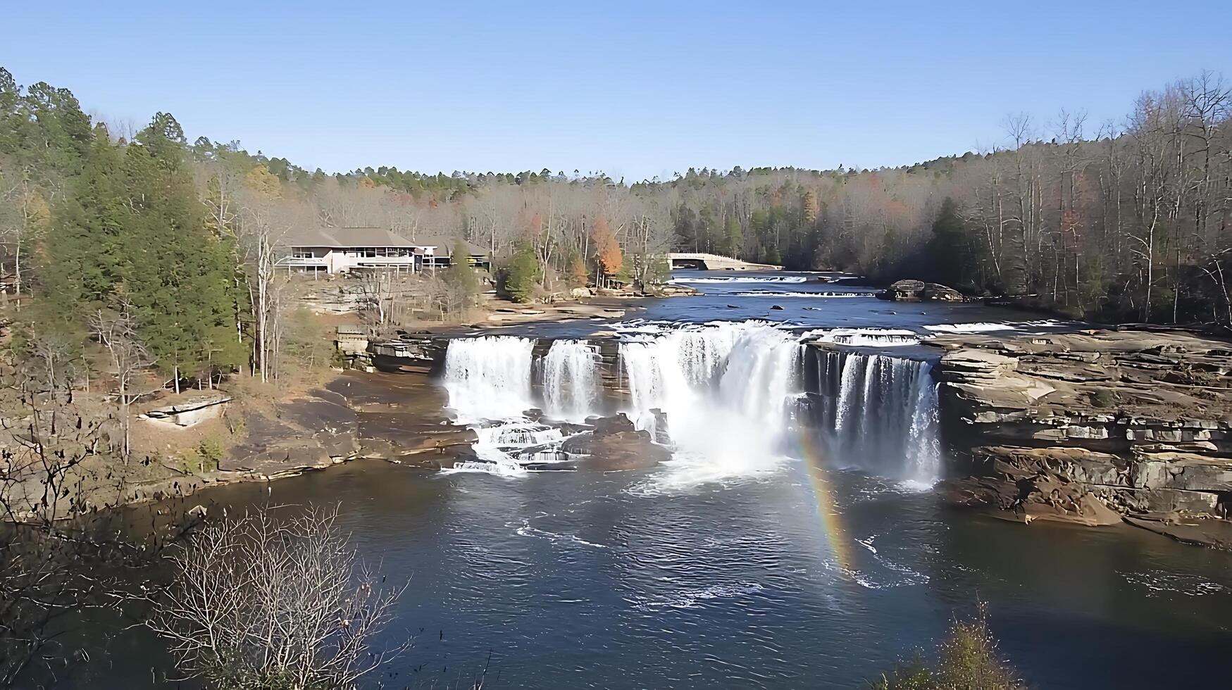 Majestic Waterfall with Rainbow and Lodge in Autumnal Landscape. A stunning panoramic view of a cascading waterfall, a nearby lodge, and a vibrant autumnal forest. photo