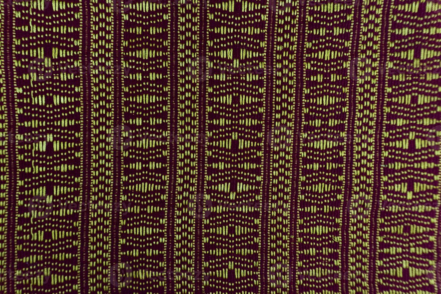 A textured fabric swatch displays vertical stripes of detailed geometric patterns in dark and light shades, revealing the fine craftsmanship of textile weaving. photo