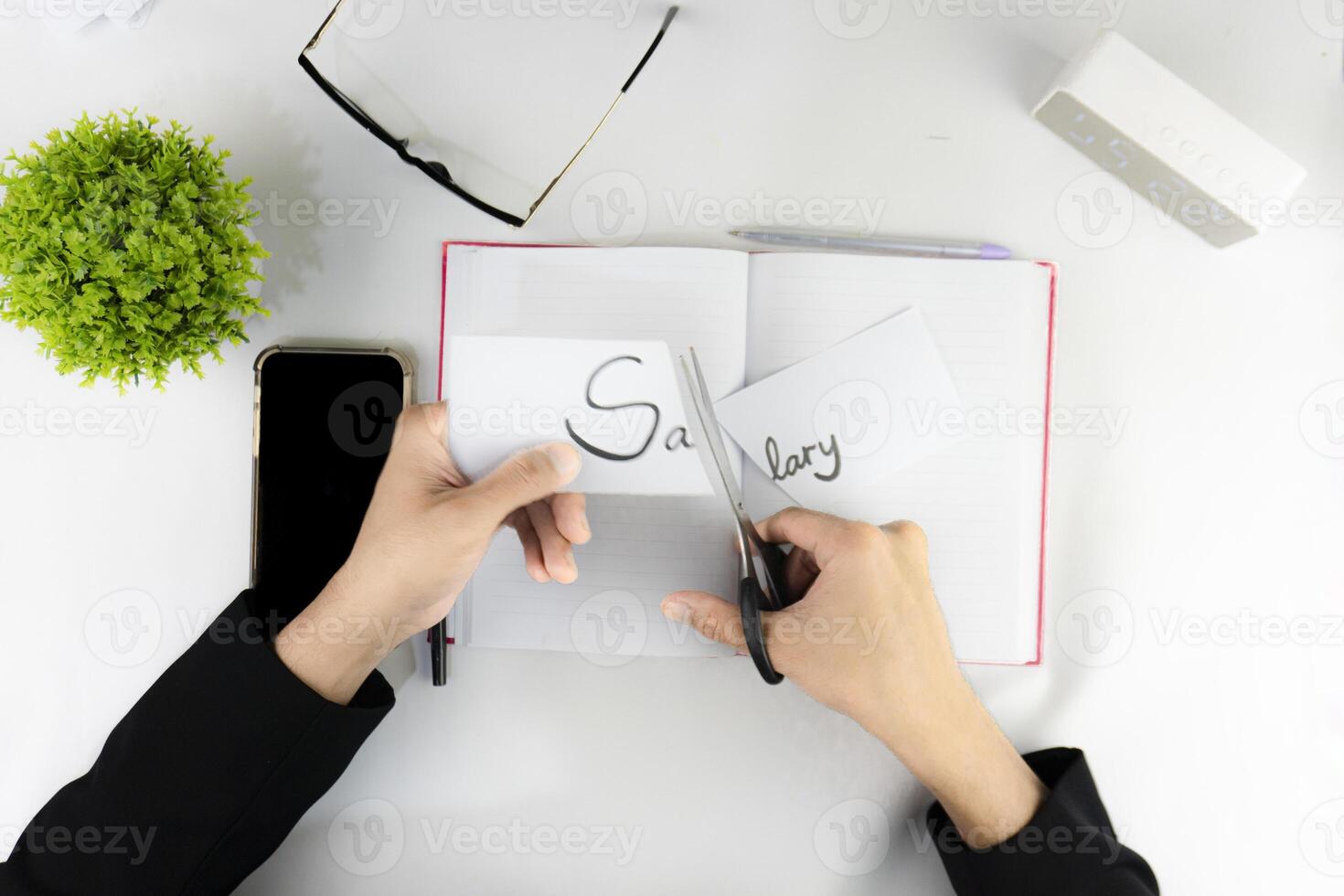 Hands cutting the word Salary with scissors on the office desk in the top view. illustration of a boss who tries to cut employee salaries photo