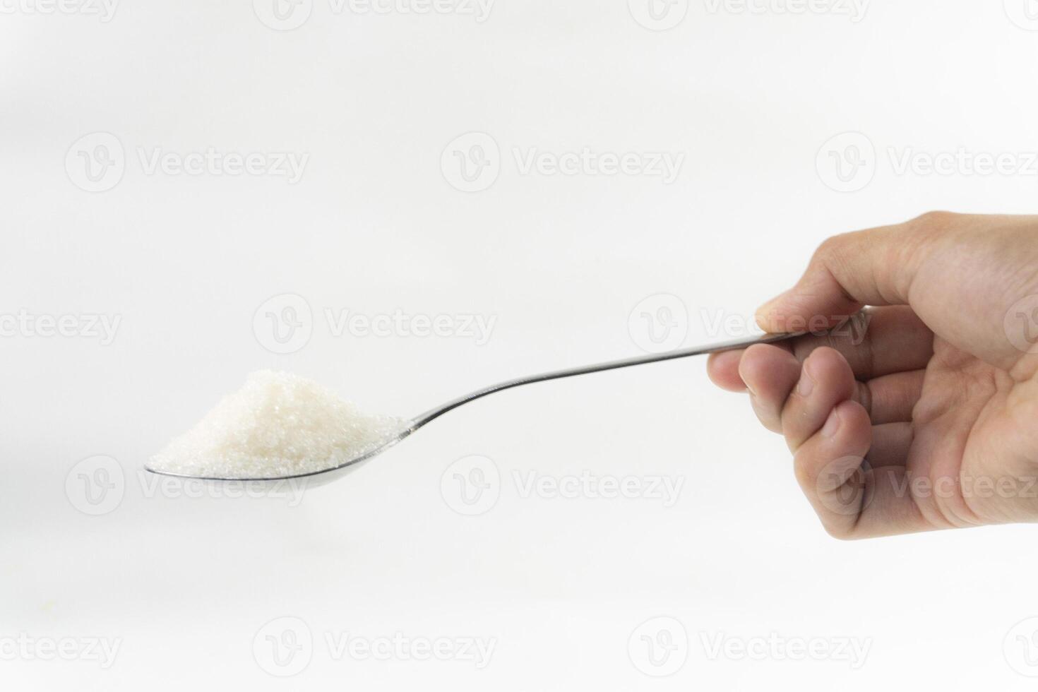 A hand holding a spoon full of sugar against a white background. photo