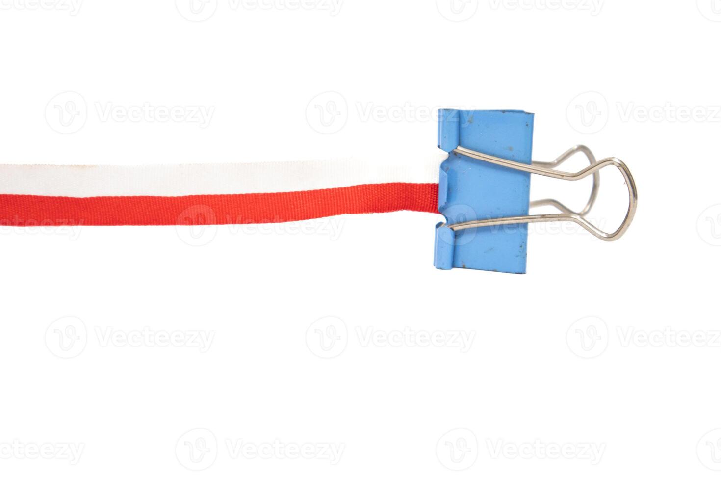 A blue binder clip holding a red and white ribbon on a white background photo