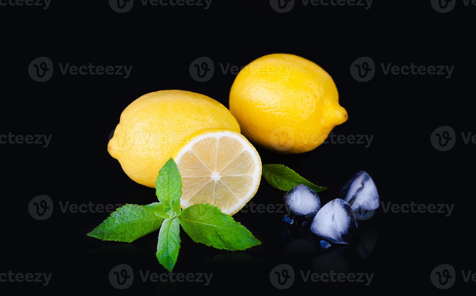 Juicy lemons, fresh mint and pieces of ice on the black background. Preparation of fresh natural lemonade. Refreshing summer drink. Close-up. photo