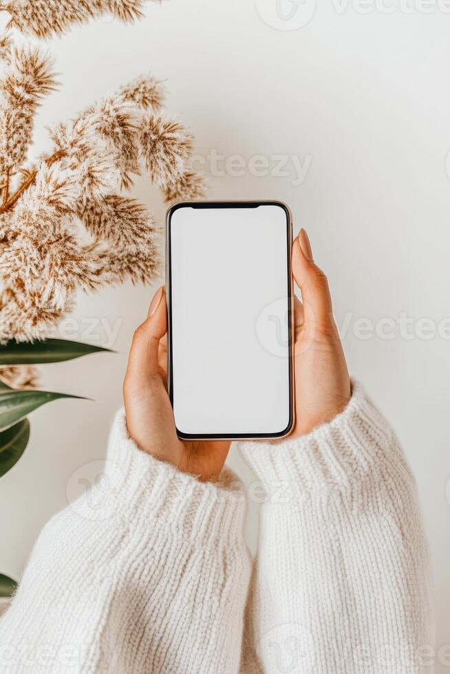 Hands hold blank screen device. Cyber security awareness concept. Neutral colors, cozy sweater, dried plant, simple background. photo